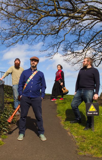The four band members next to a 'sheer drop' sign
