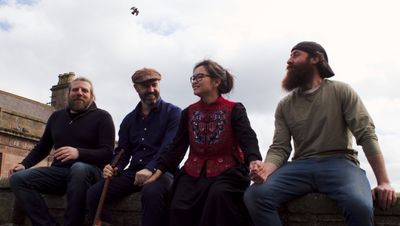 The four band members sitting on a fence