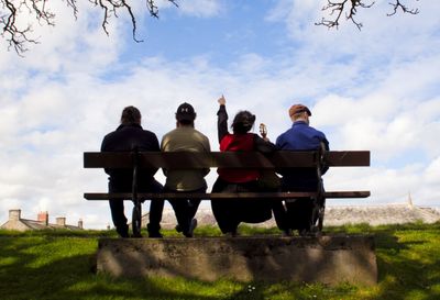 The four band members sitting on a bench, viewed from behind